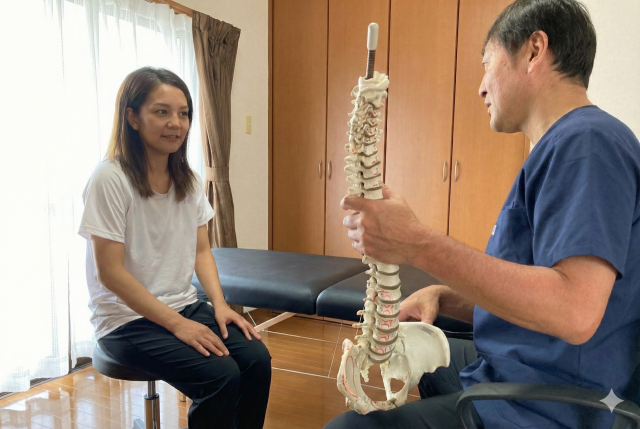 理学療法士・作業療法士の川端代表が、患者様に骨模型で体の歪みを説明している様子（うるま市）