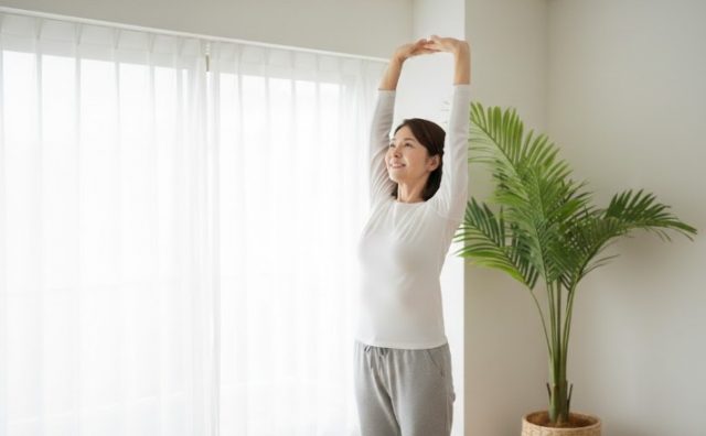 朝の腰痛が改善し、明るい日差しの中で心地よく背伸びをする50代女性のイメージ。うるま市で慢性腰痛にお悩みの方への施術事例